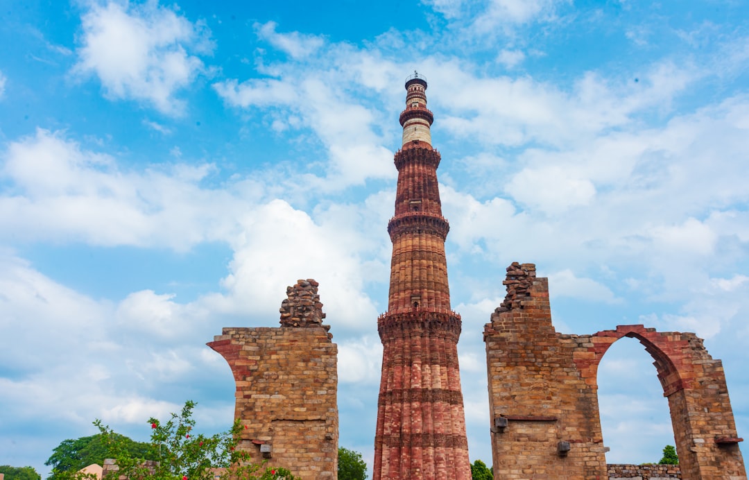 Qutub minar tower against a cloudy blue sky